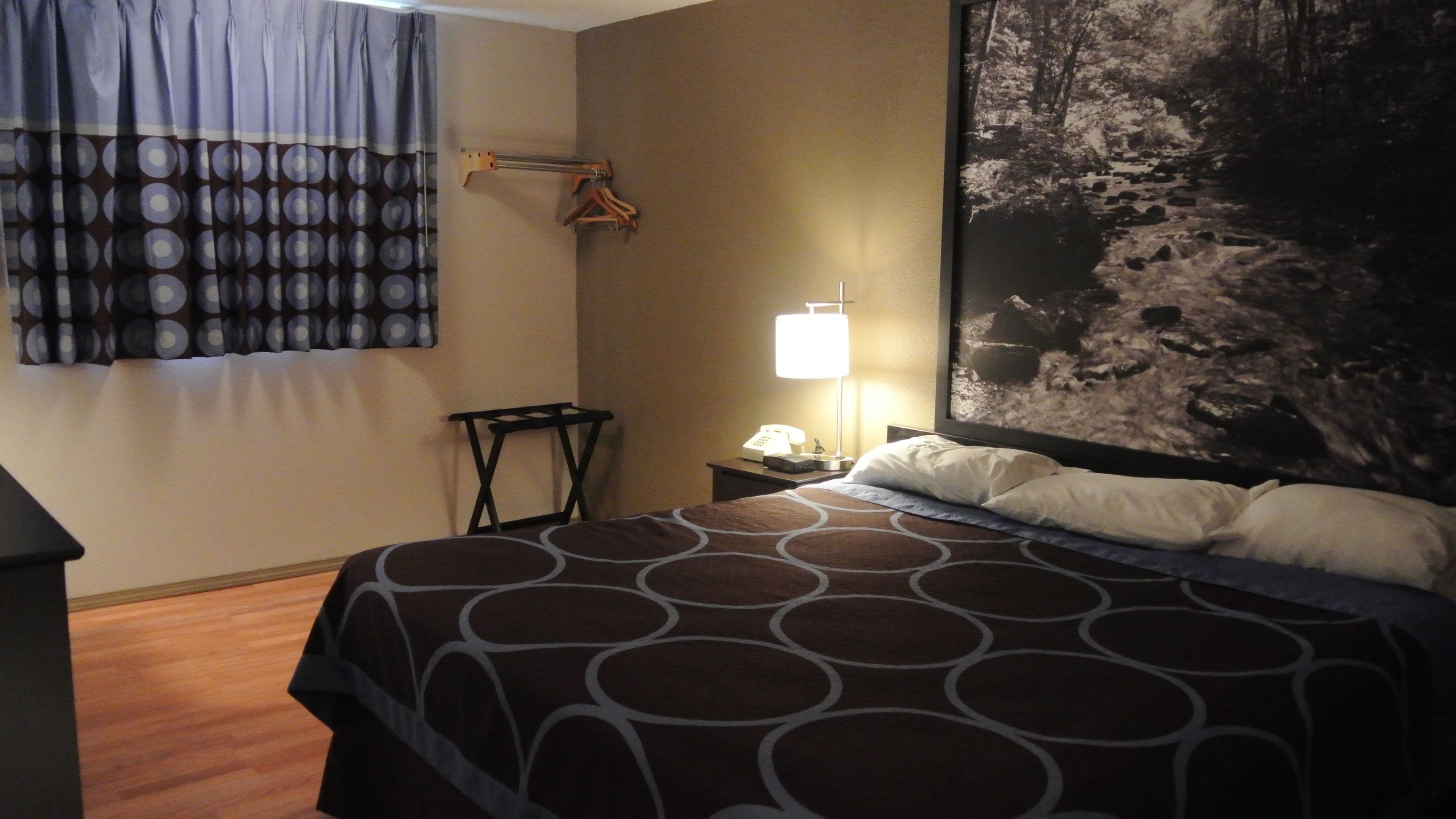 Habitación de hotel con una cama, una mesita de noche con lámpara, un teléfono y un perchero en la pared.