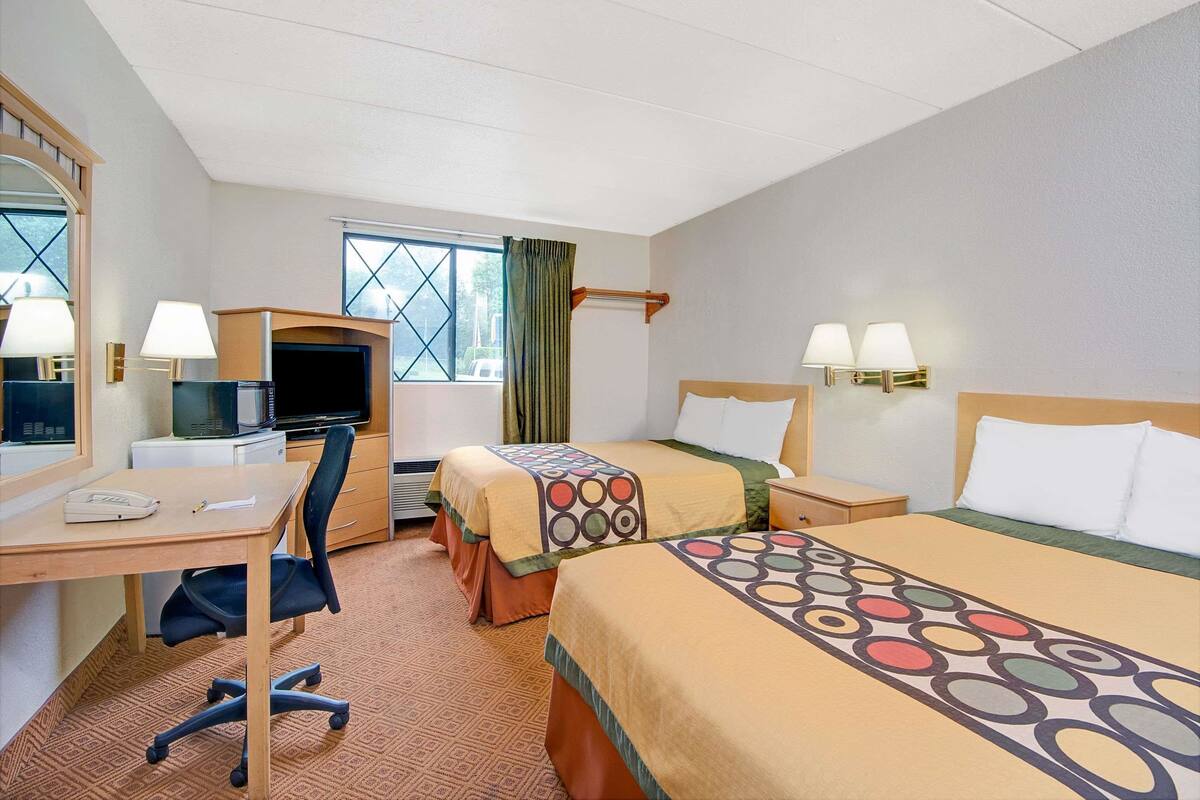 Une chambre d’hôtel avec deux lits, un bureau, une chaise, une télévision et une fenêtre avec des rideaux.