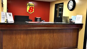 Un hall d’hôtel avec un comptoir d  ’accueil en bois, le logo Super 8 sur le mur, une horloge et un paillasson orné du logo Super 8 et de l’inscription « Stamford, CT ».