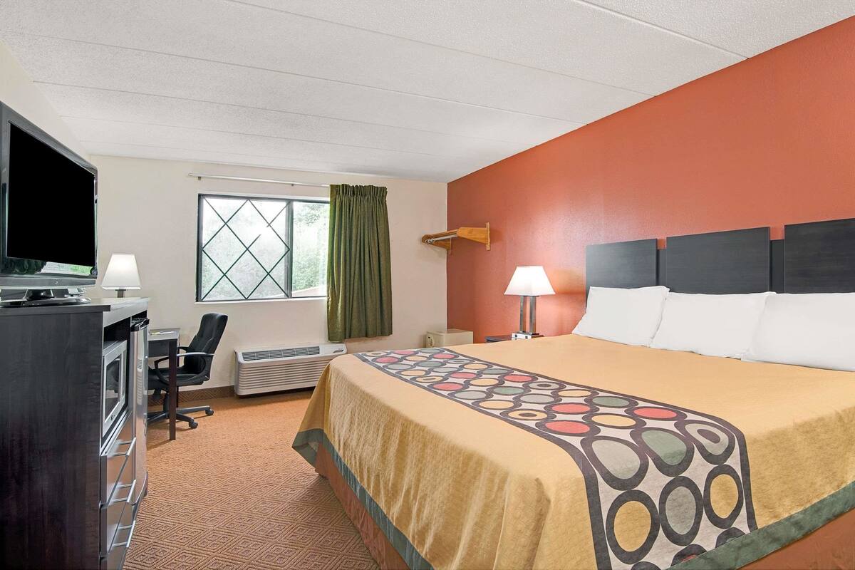 Une chambre d’hôtel avec un lit, un bureau avec un ordinateur, une télévision et une fenêtre avec des rideaux.