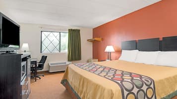 A hotel room with a bed, a desk with a computer, a TV, and a window with curtains.
