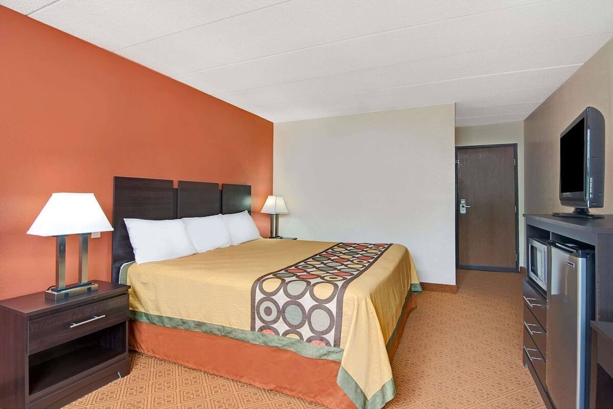 Une chambre d’hôtel comprenant un lit, deux tables de chevet avec lampes, une télévision et un mini-bar.