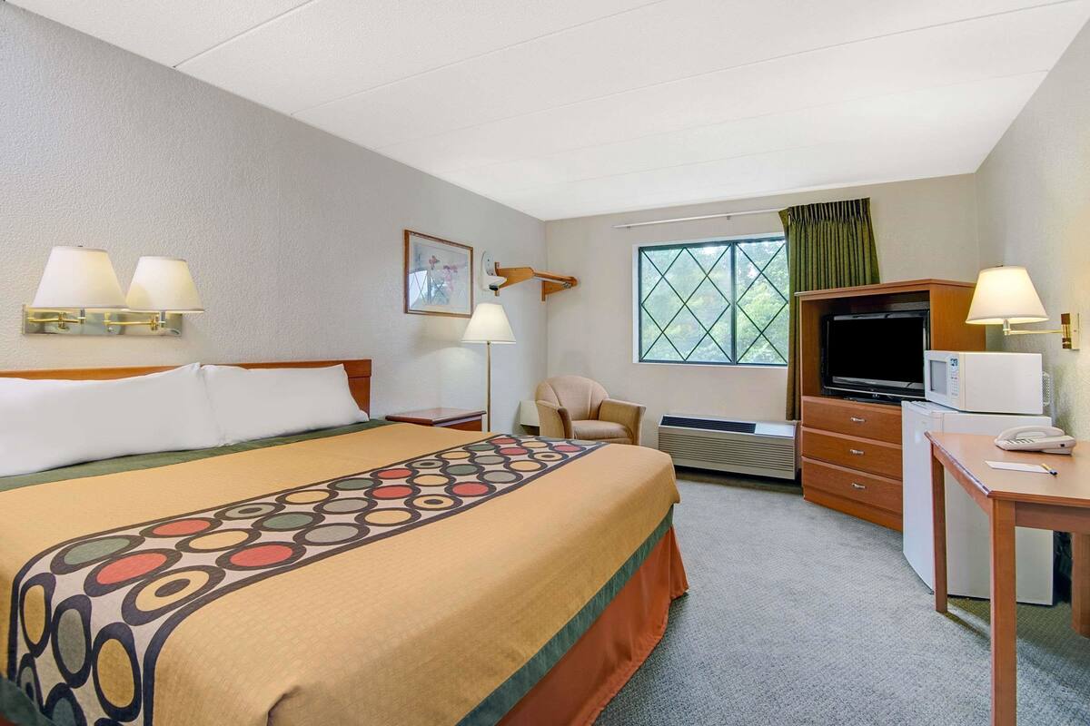 Une chambre d’hôtel avec un grand lit, un bureau avec un téléphone, une télévision et une fenêtre avec des rideaux.