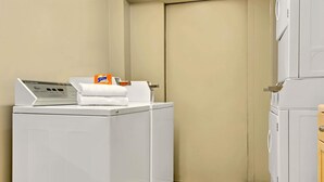 Une buanderie équipée de deux machines à laver blanches, d’une pile de serviettes blanches et d’une boîte de lessive Sun.