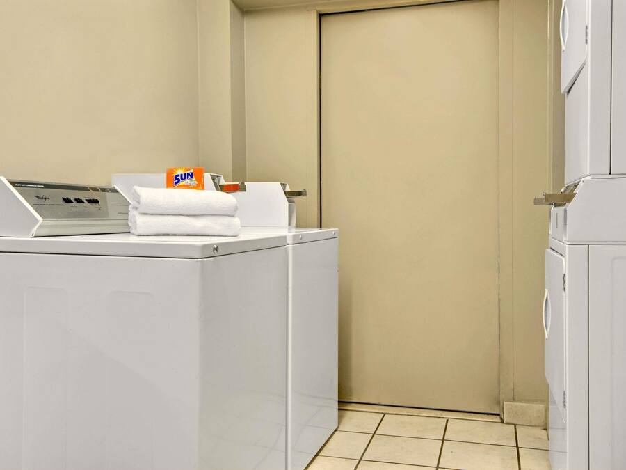 A laundry area with two white washing machines, a stack of white towels, and a box of Sun laundry detergent.