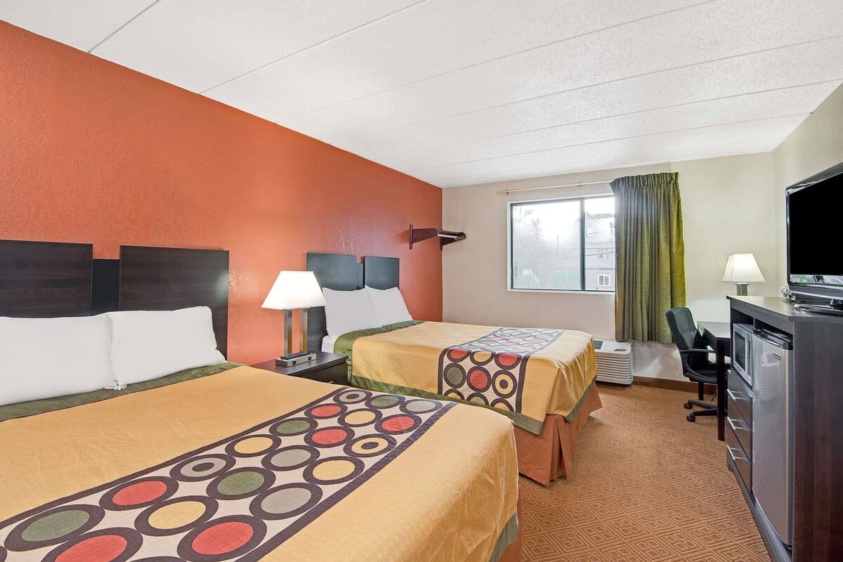 Une chambre d’hôtel avec deux lits, un bureau, une chaise et un téléviseur.