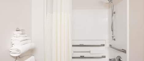 A modern bathroom with a shower, a towel rack with folded towels, and a glass shower door.