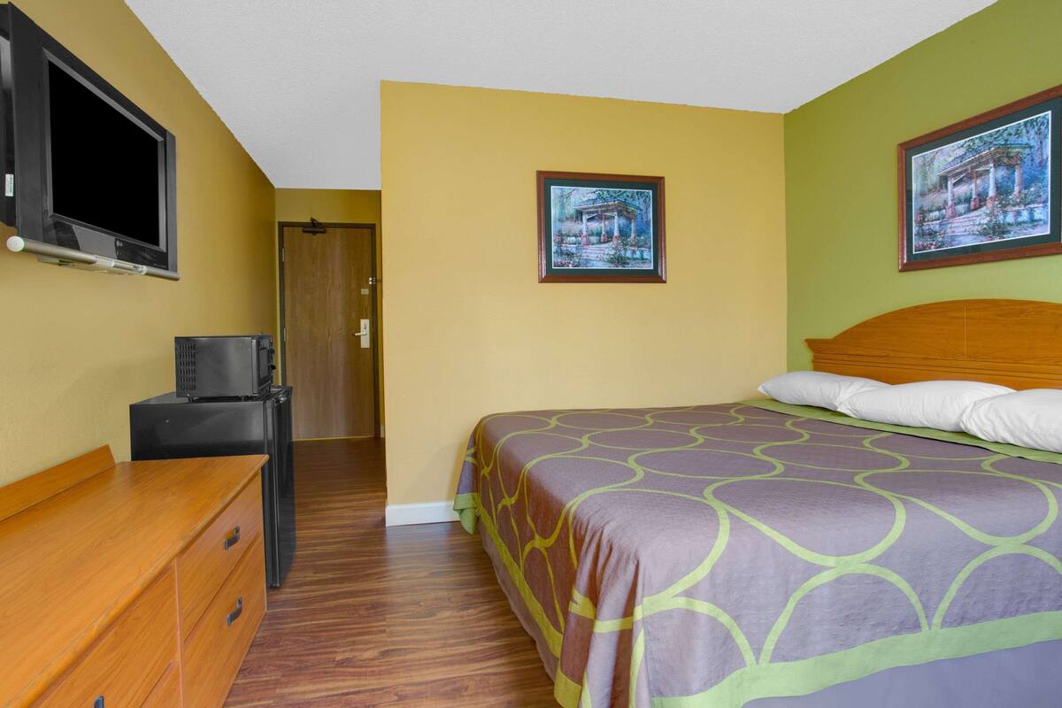 A bedroom with a bed, a dresser, a television, and a door.