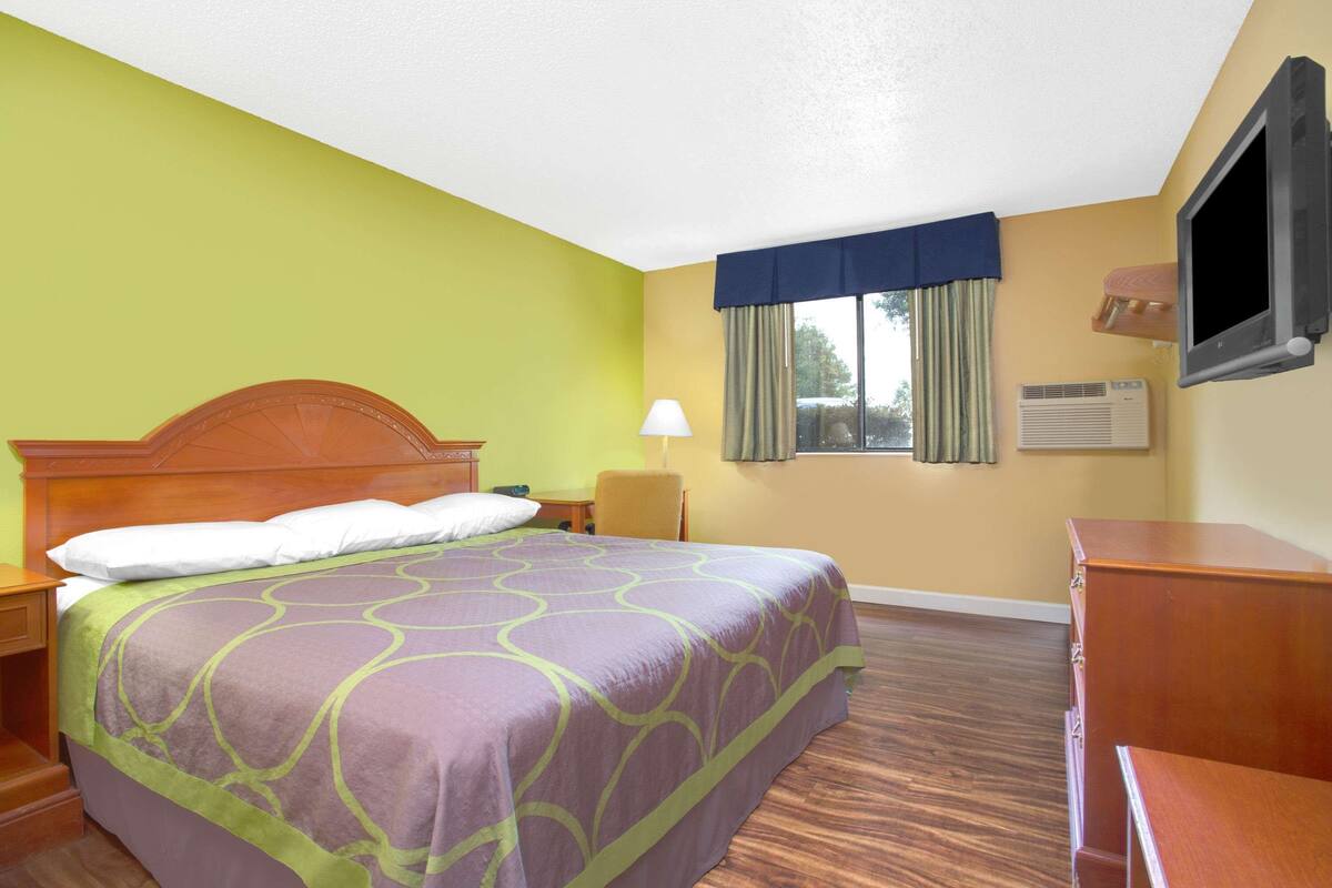 A hotel room with a bed, a desk, a chair, a TV, and a window with curtains.
