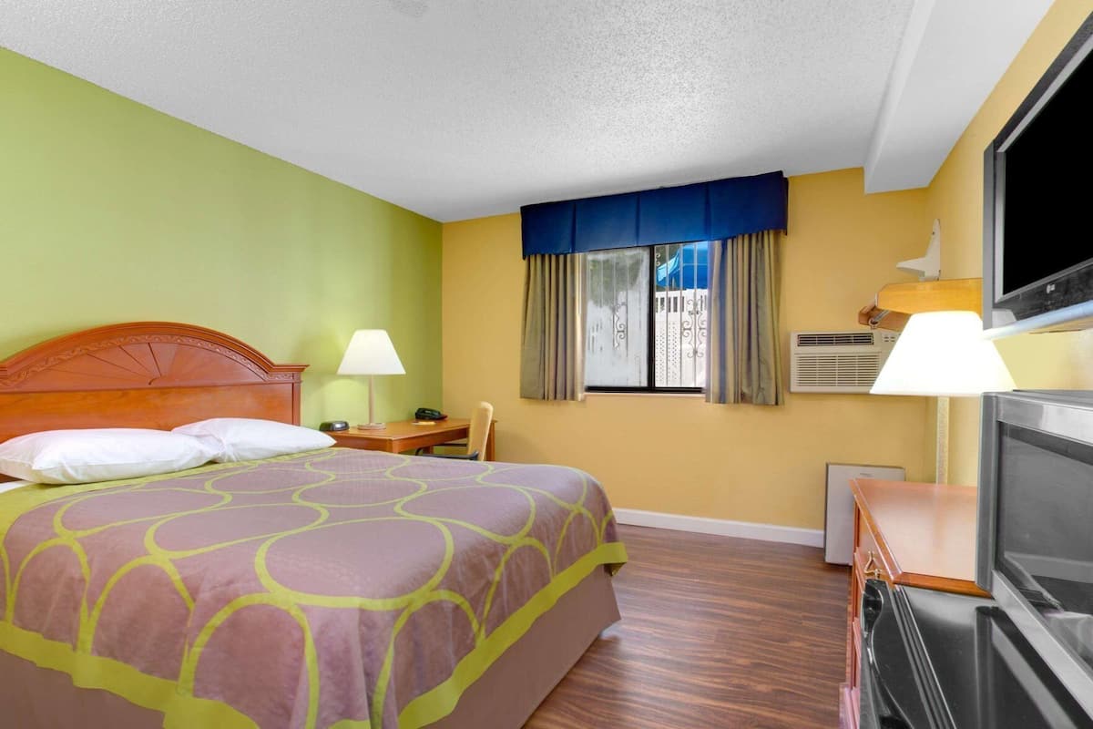 A hotel room with a bed, a desk, a TV, and a window with curtains.