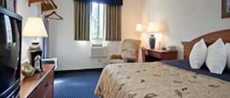 Habitación de hotel con cama, escritorio con lámpara, silla, televisor y ventana con cortinas.
