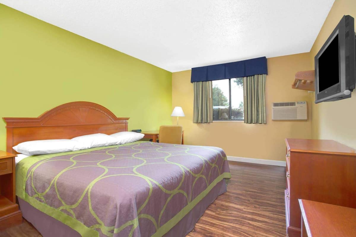 A hotel room with a bed, a desk, a chair, a TV, and a window with curtains.