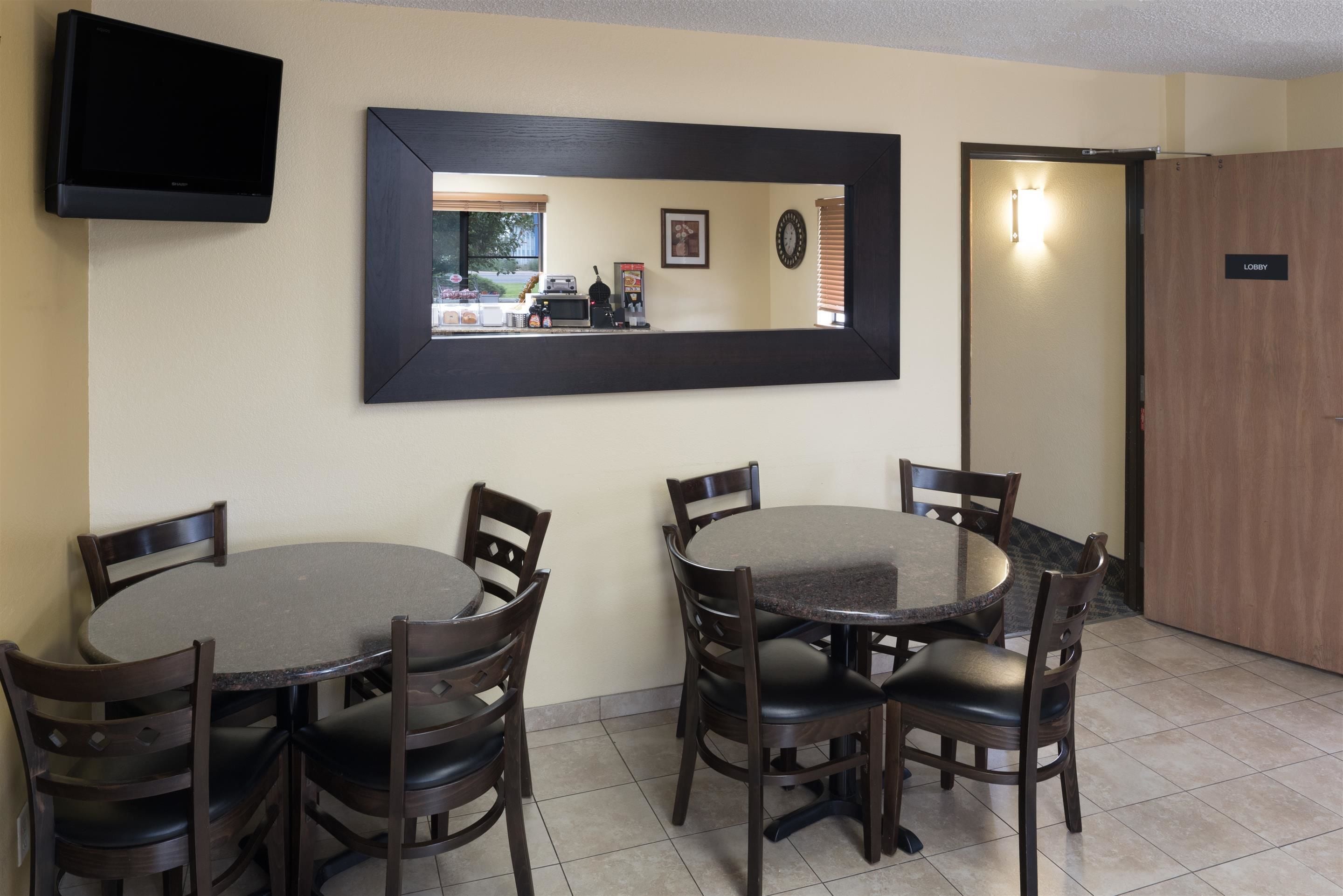Un coin repas avec deux tables rondes et des chaises, un téléviseur à écran plat fixé au mur et un miroir encadré qui reflète la pièce.