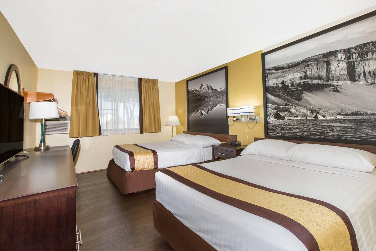 A hotel room with two beds, a desk, a TV, and a large framed picture on the wall.