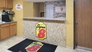 Un espace d’accueil d’hôtel avec un comptoir en granit, le logo de la chaîne Super 8, un panneau d’accueil et un paillasson.