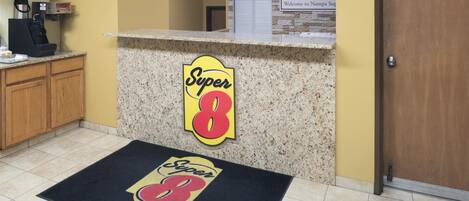 A hotel reception area with a granite counter, a Super 8 logo, a welcome sign, and a doormat.