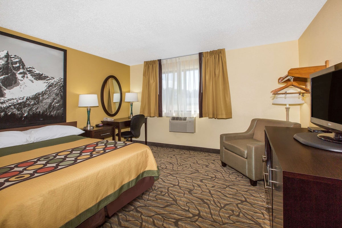 A hotel room with a bed, two bedside tables with lamps, a desk with a chair, a television, and a large window with curtains.