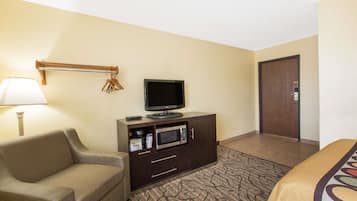 Una habitación de hotel con sofá, televisión sobre un mueble, microondas y una puerta.