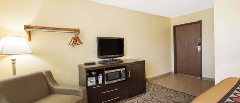 Una habitación de hotel con sofá, televisión sobre un mueble, microondas y una puerta.