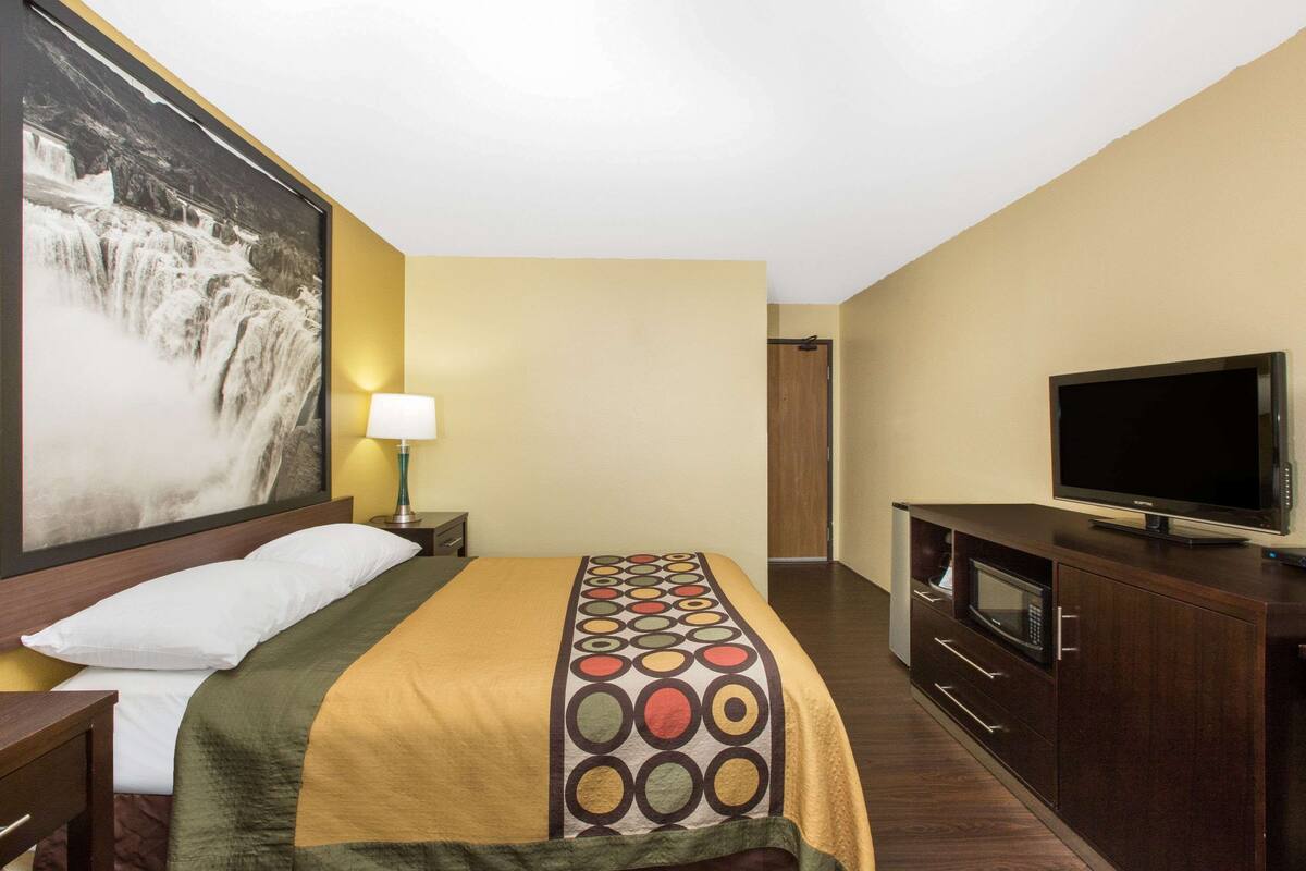 A hotel room with a bed, a TV, a microwave, and a large painting on the wall.