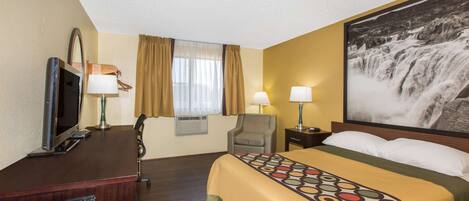 Una habitación de hotel con cama, escritorio, televisión, dos lámparas, una silla y un ventanal con cortinas.