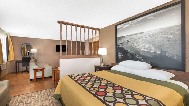 Une chambre d’hôtel avec un grand lit, un bureau, une chaise, un miroir et un tableau représentant un paysage.