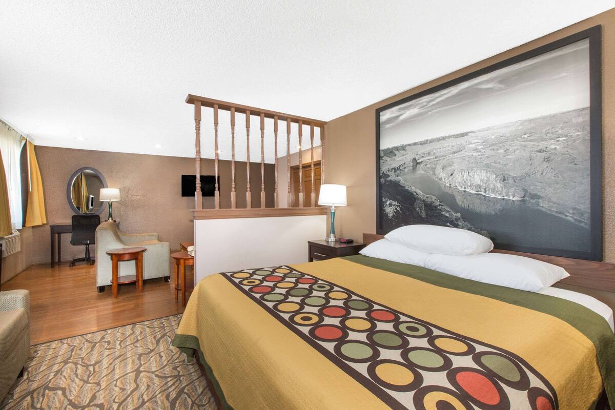 A hotel room with a large bed, a desk, a chair, a mirror, and a painting of a landscape.