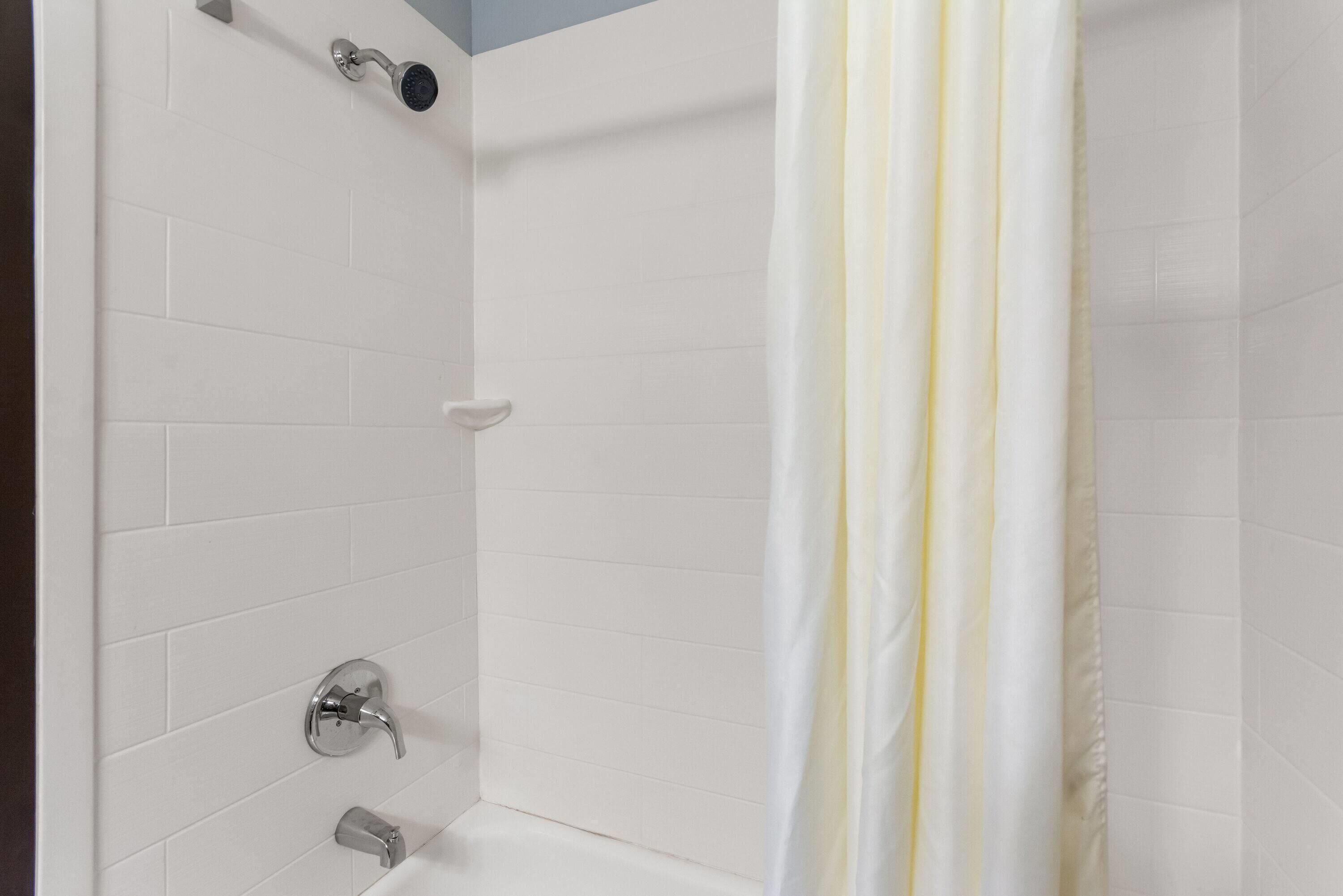 Ducha con azulejos blancos, cortina blanca y cabezal de ducha cromado.