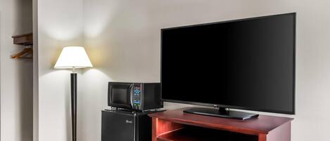 A hotel room with a flat-screen TV, a microwave, a refrigerator, and a lamp.
