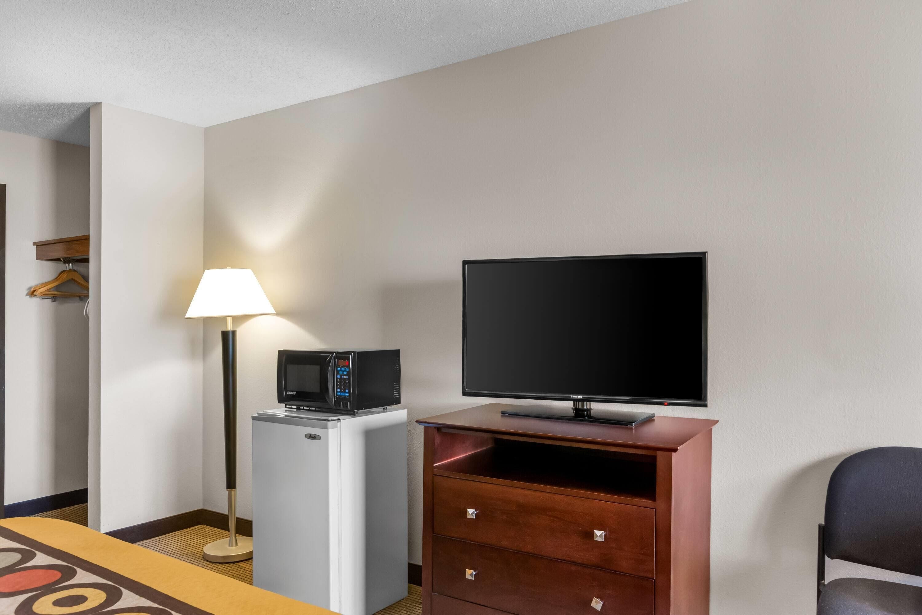 Habitación de hotel con televisor de pantalla plana, microondas, lámpara, cómoda y una silla.
