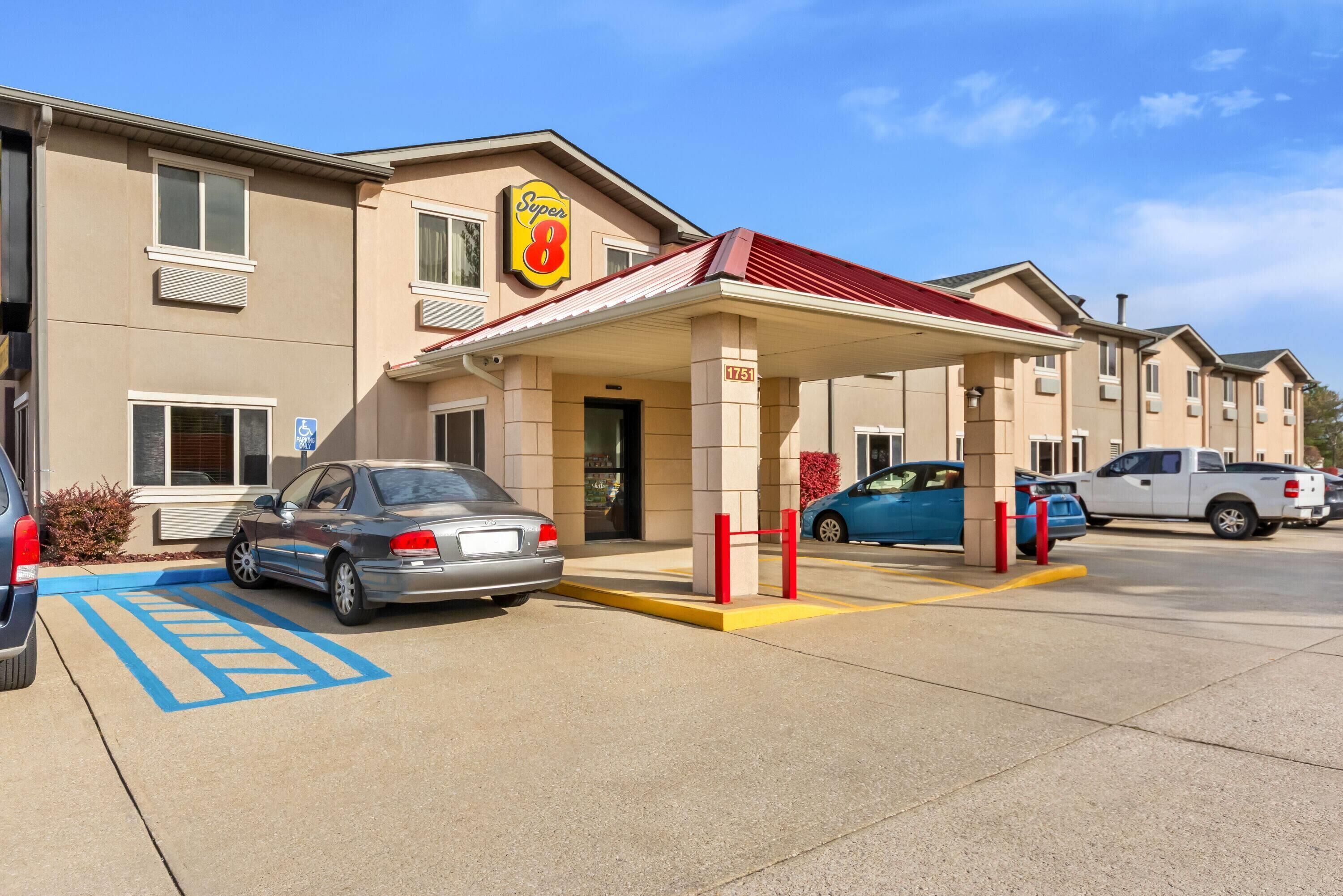 A hotel with a red awning, a parking lot, and a blue handicapped parking sign.