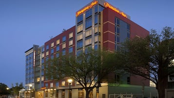 A multi-story hotel with a prominent "Hampton Inn" sign, large windows, and a well-lit facade.
