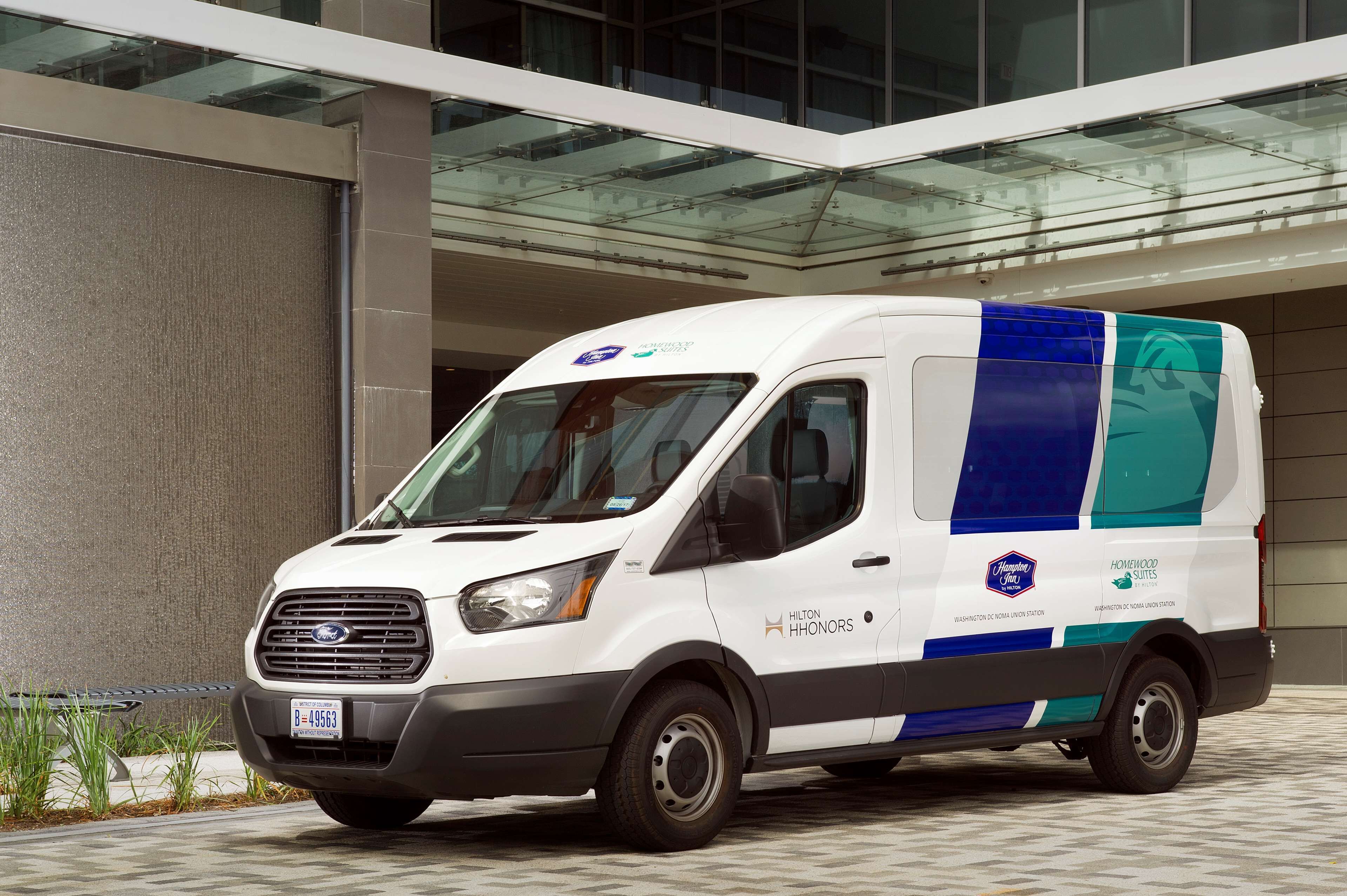 A white van with blue and green stripes parked in front of a building with a glass roof.