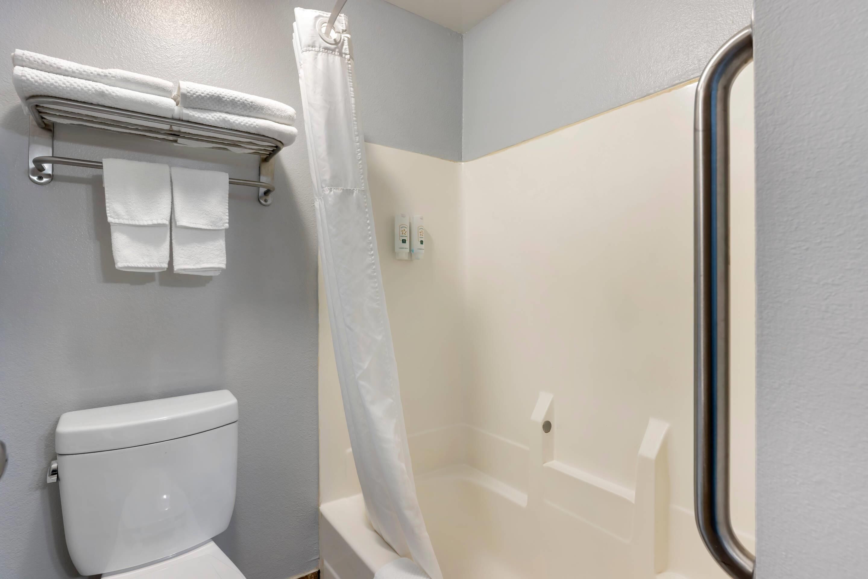 Un baño con inodoro, toallero con toallas dobladas, cortina de ducha y bañera.