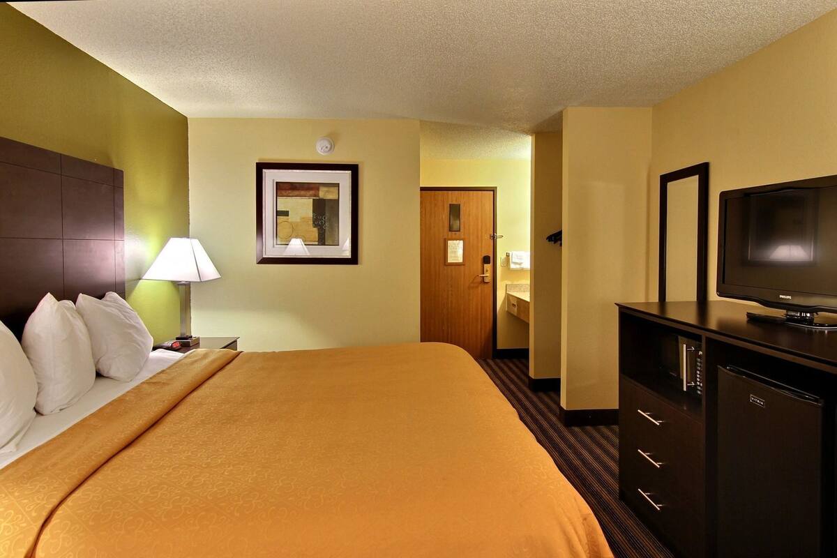 A hotel room with a bed, a television, a desk, and a door.