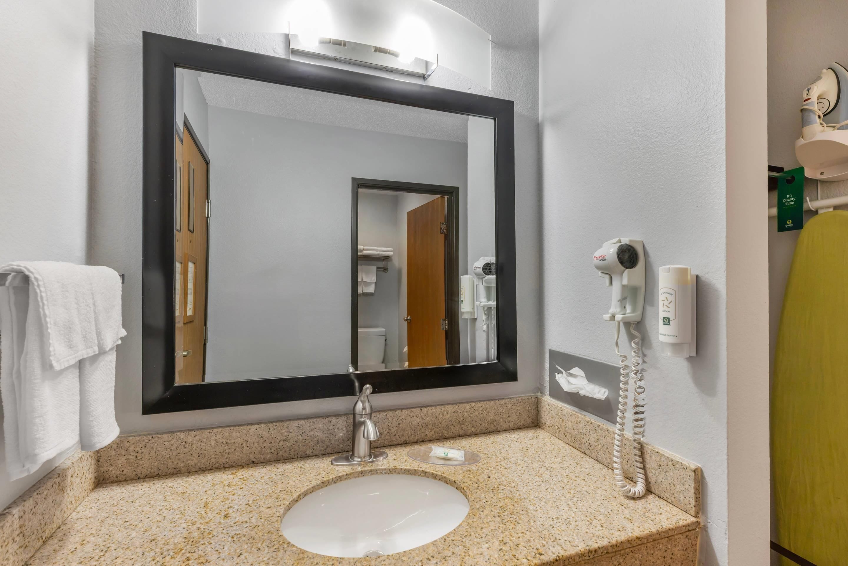 Un bagno con uno specchio grande, un lavandino, un asciugacapelli e un telefono.