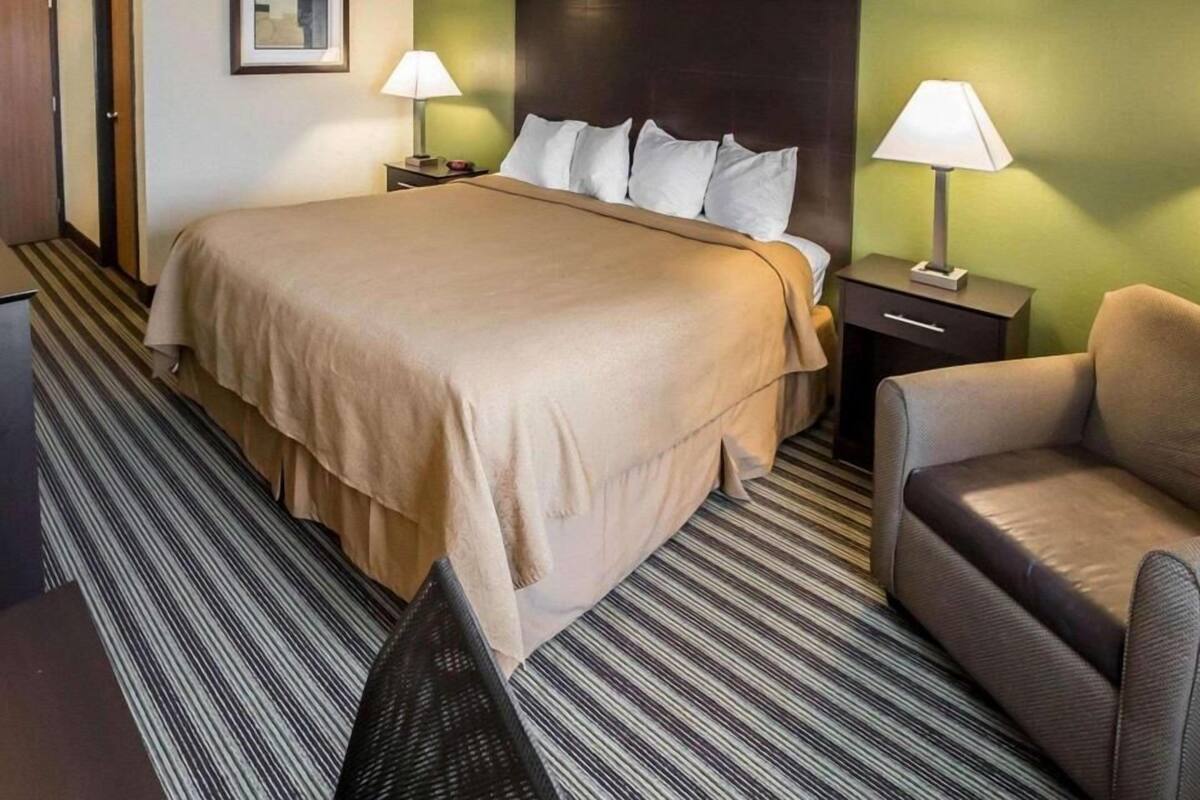 A hotel room with a large bed, two bedside tables with lamps, a chair, and a framed picture on the wall.