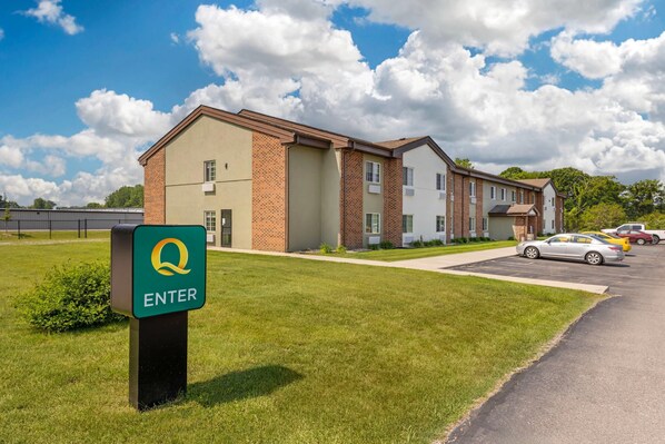 A building with a green 'Q' entrance sign, a parking lot, and a clear sky. - Quality Inn Chesterton near Indiana Dunes National Park I-94 (Chesterton)