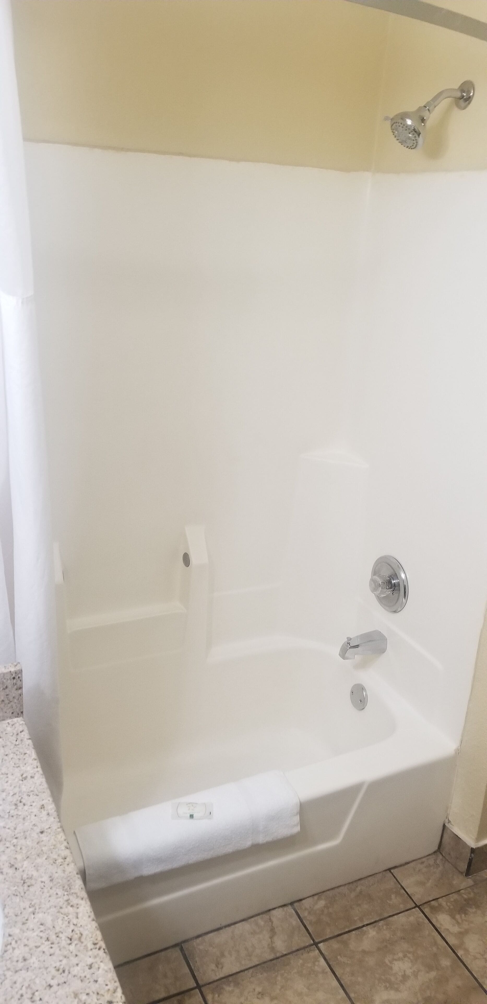 Une baignoire blanche équipée d’un pommeau de douche, d’un robinet et d’une petite étagère.