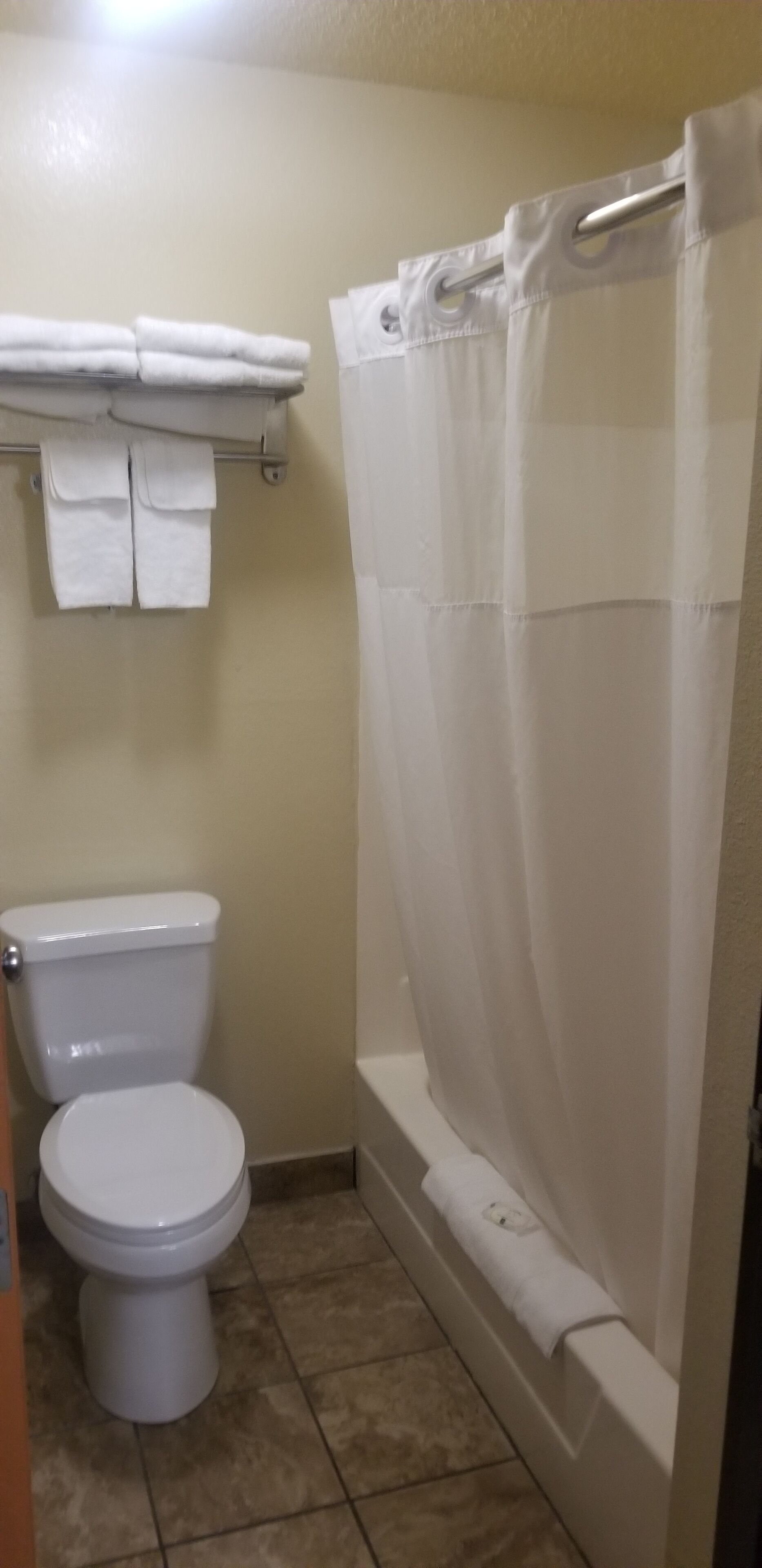 A bathroom with a toilet, a shower curtain, and a towel rack with towels.
