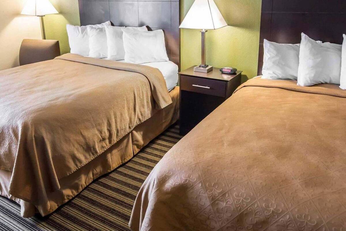 A hotel room with two beds, a headboard, nightstands, lamps, and a clock.