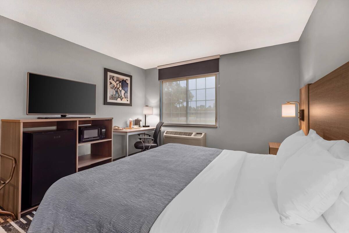A hotel room with a bed, a desk with a computer, a television, and a window with blinds.