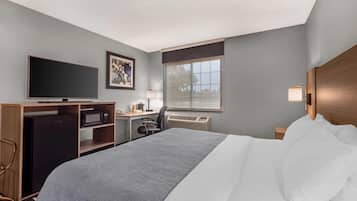 A hotel room with a bed, a desk with a computer, a television, and a window with blinds.