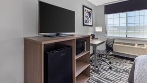 Quarto de hotel com televisão de tela plana, minibar, micro-ondas, escrivaninha com cadeira e uma janela grande com vista.