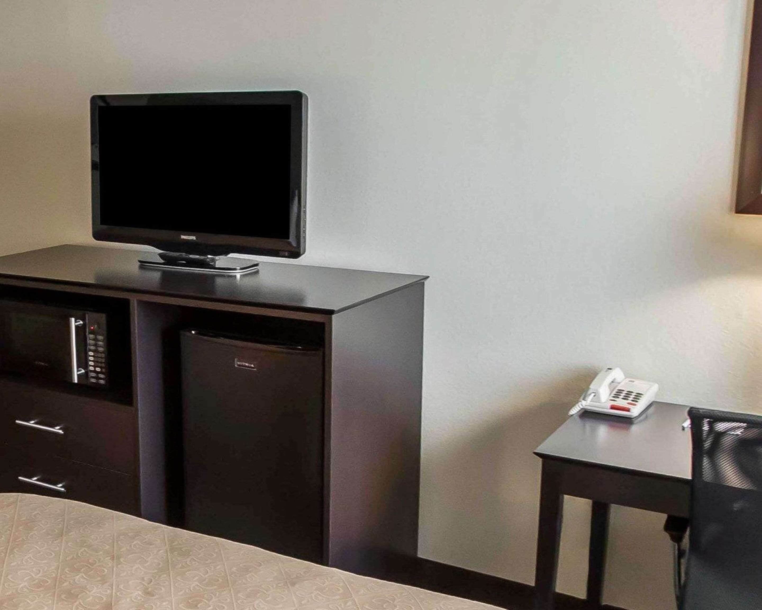 Une chambre d’hôtel compacte équipée d’un téléviseur à écran plat posé sur un meuble, d’un four à micro-ondes et d’une petite table avec un téléphone.