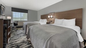 Quarto de hotel com duas camas, uma escrivaninha, uma cadeira e uma janela grande.