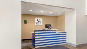 Uma receção com design listrado em azul e branco, um letreiro com a inscrição "Quality by Choice Hotels" e um ecrã digital.