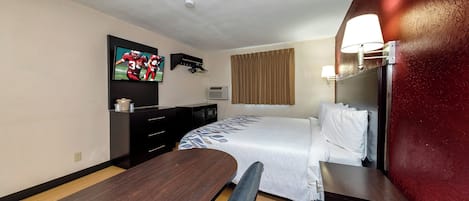A hotel room with a bed, a desk, a chair, a TV mounted on the wall, and a window with curtains.