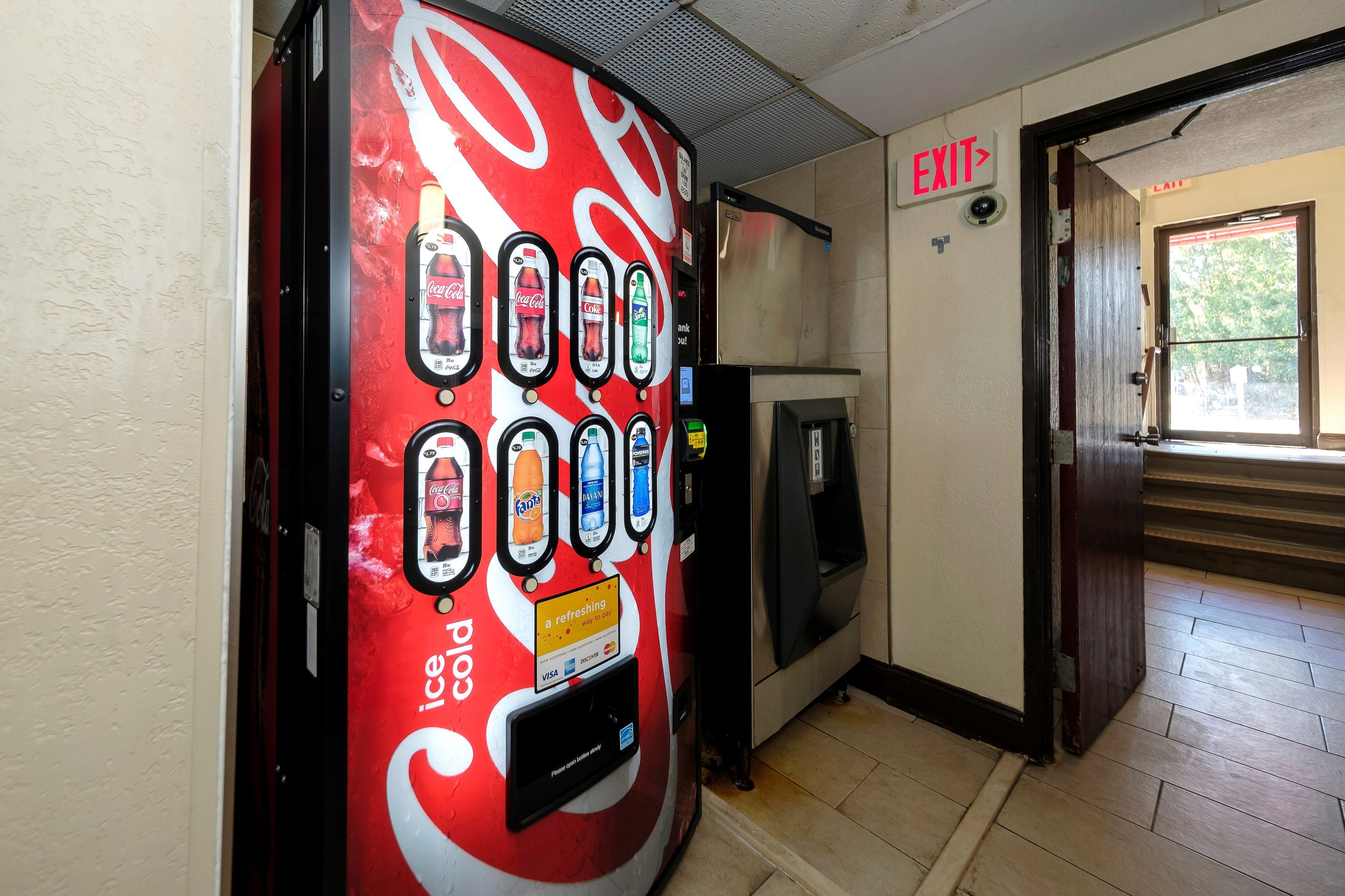 A vending machine with various beverage options, an exit sign, and a door leading outside.