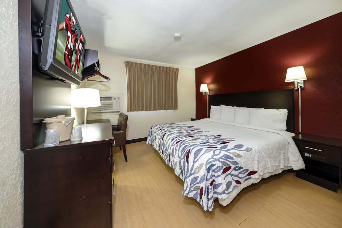 A hotel room with a bed, a desk, a chair, a TV mounted on the wall, and two bedside lamps.